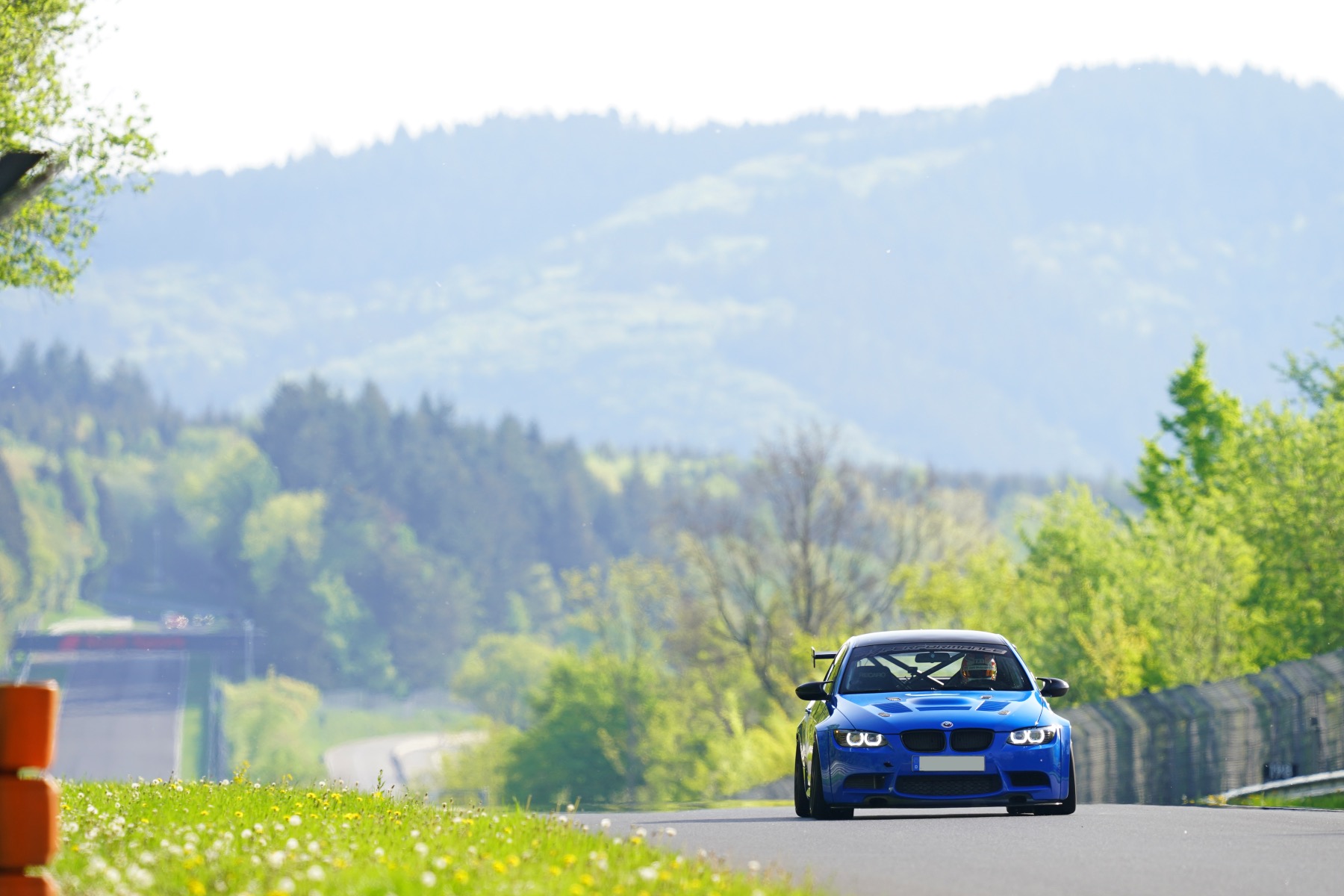 A blue E92 M3 on track with the Eifel mountains and countryside in the background.